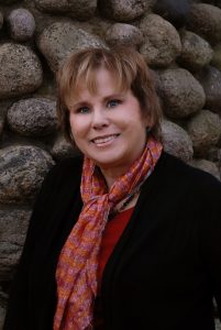 Headshot of Christine Lajewski smiling. She has short brown hair and is wearing a black jacket and a scarf with fall colores.