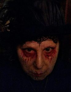 A woman is wearing scary Halloween makeup and is in front of a dark background.