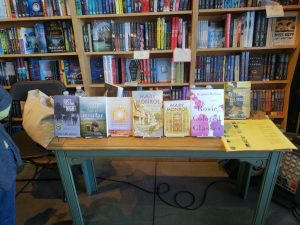 Books on a table in front of a book shelf.