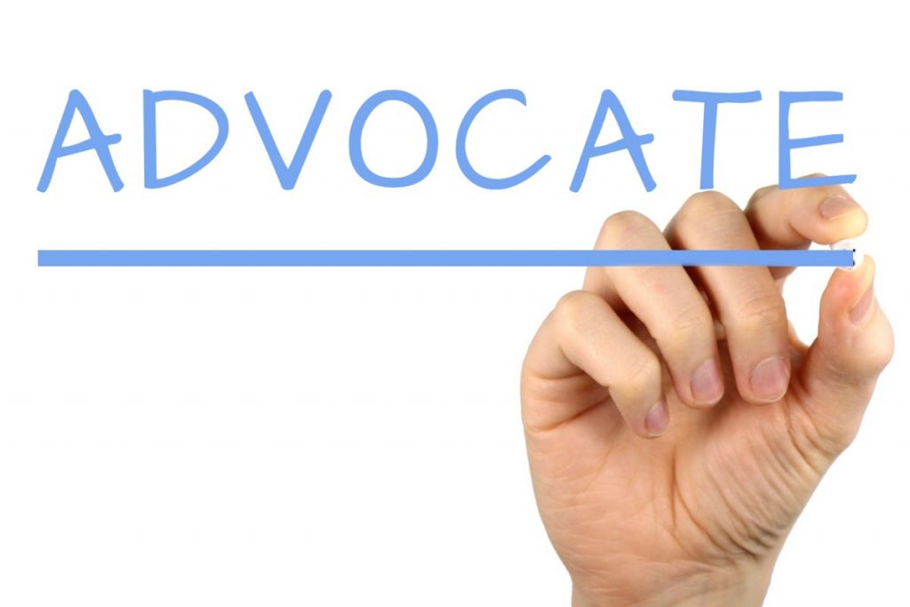 A hand is writing out ADVOCATE.